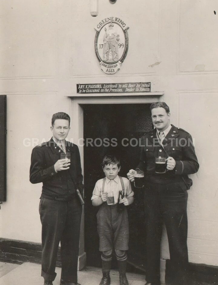 Major Thomas B. McCray and Captain Arlo Anderson from the 479th Fighter Group at Wattisham pose with a local boy outside a pub in Brent Eleigh, 1945.